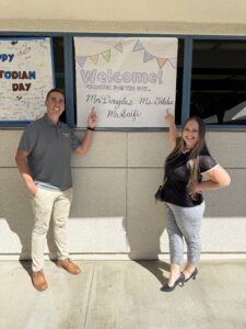 Joel Douglass and Brittnie Gildea of Rowland Water District pointing at the 'Principal for a Day' welcome banner. 